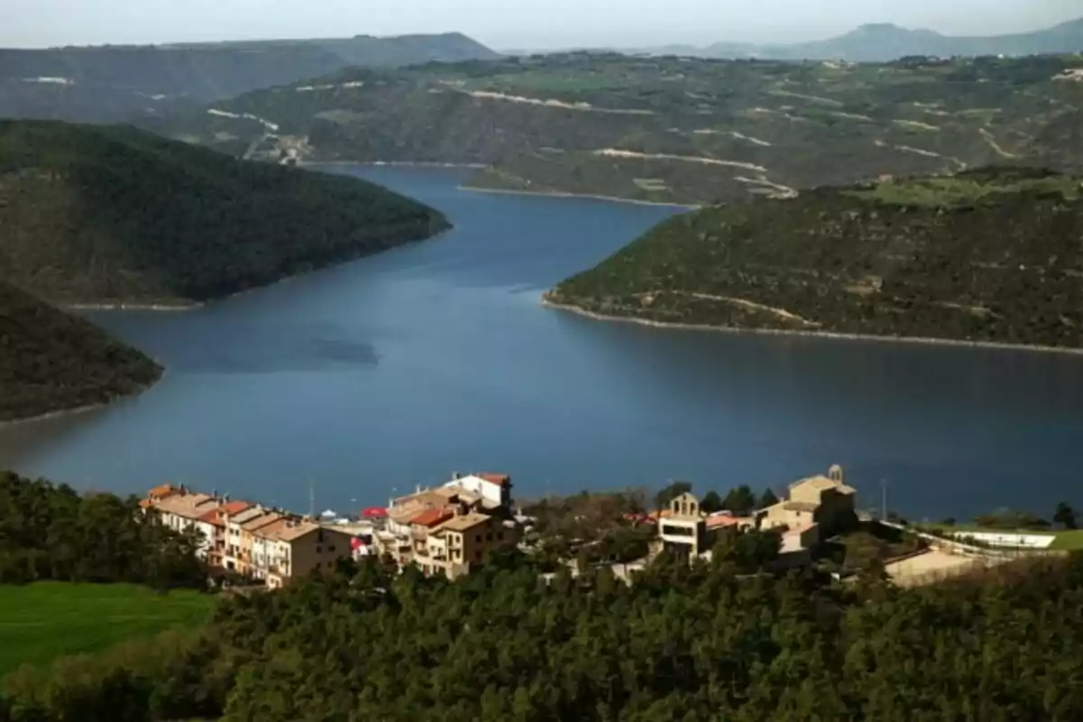 Vista panoràmica d´un llac envoltat de turons verds amb un petit poble en primer pla.