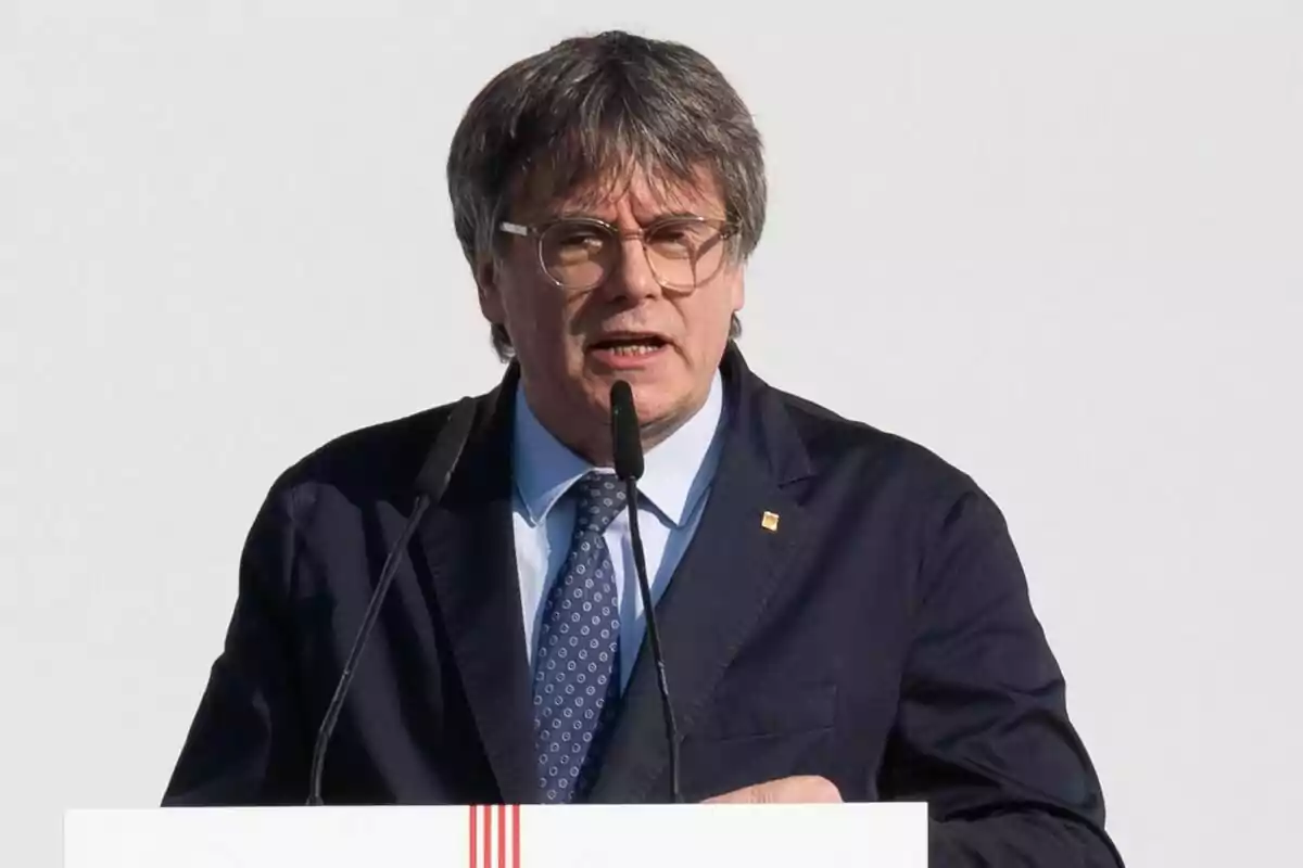 Carles Puigdemont amb vestit fosc parlant en un podi amb micròfons.