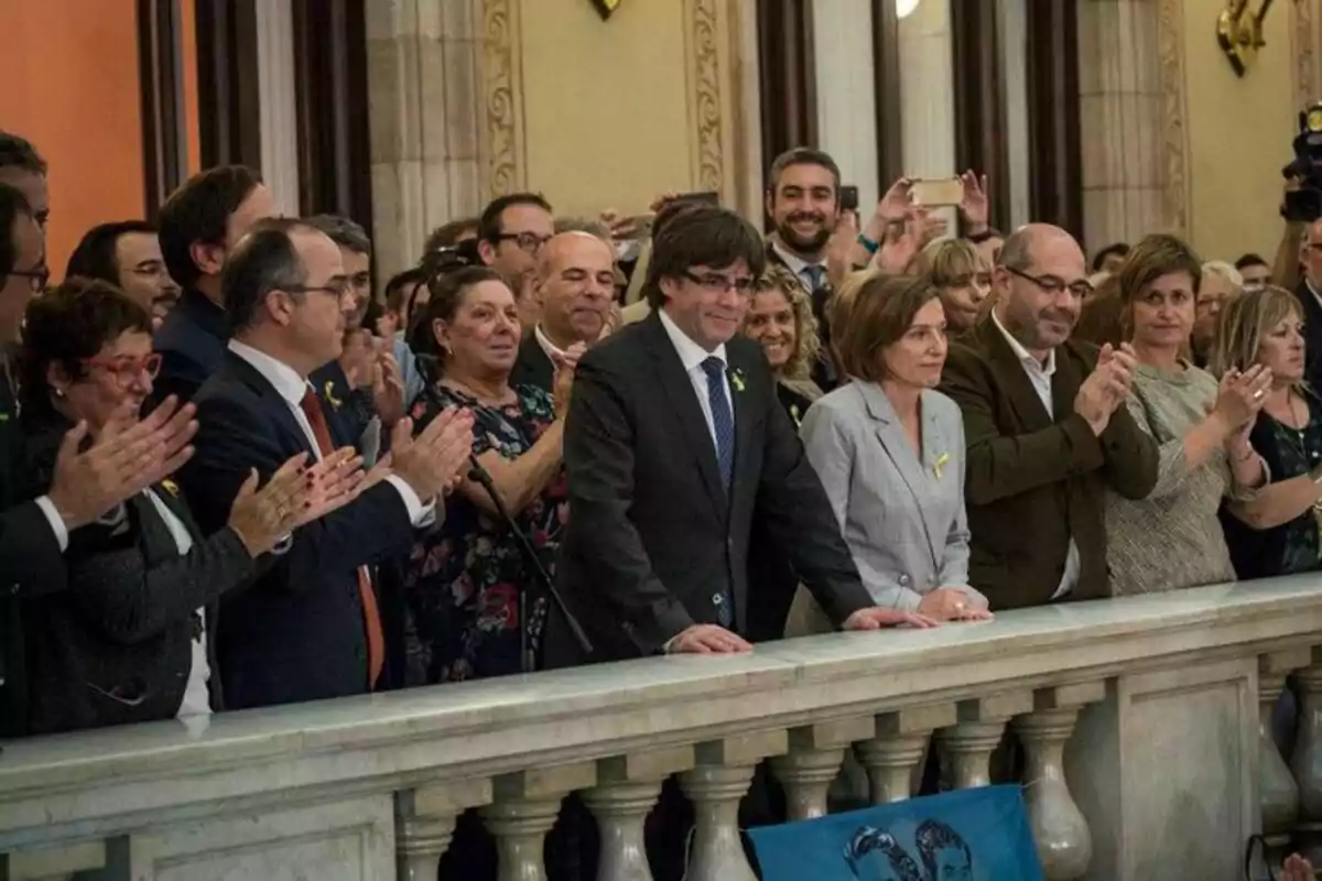 Un grup de persones aplaudeixen en un esdeveniment formal en un edifici amb columnes i decoració clàssica.