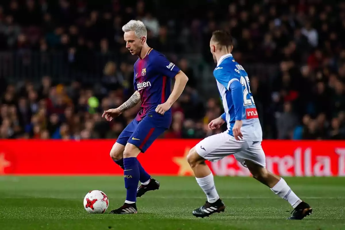 A Barcelona player controls the ball while an Espanyol opponent marks him during a soccer match in a stadium full of spectators. A Barcelona player controls the ball while an Espanyol opponent marks him during a soccer match in a stadium full of spectators.