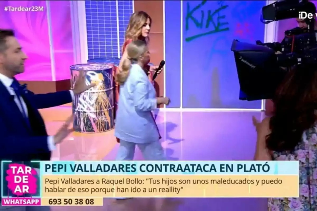 En un plató de televisió de Tardear amb llums de colors, diverses persones interactuen mentre una càmera grava l'escena. Frank Blanco amb vestit blau sembla estar gesticulant, mentre Verónica Dulanto i Pepi Valladares caminen a prop d'un barril decoratiu. A la part inferior, hi ha un text que menciona un conflicte entre Pepi Valladares i Raquel Bollo. En un plató de televisió de Tardear amb llums de colors, diverses persones interactuen mentre una càmera grava l'escena. Frank Blanco amb vestit blau sembla estar gesticulant, mentre Verónica Dulanto i Pepi Valladares caminen a prop d'un barril decoratiu. A la part inferior, hi ha un text que menciona un conflicte entre Pepi Valladares i Raquel Bollo.