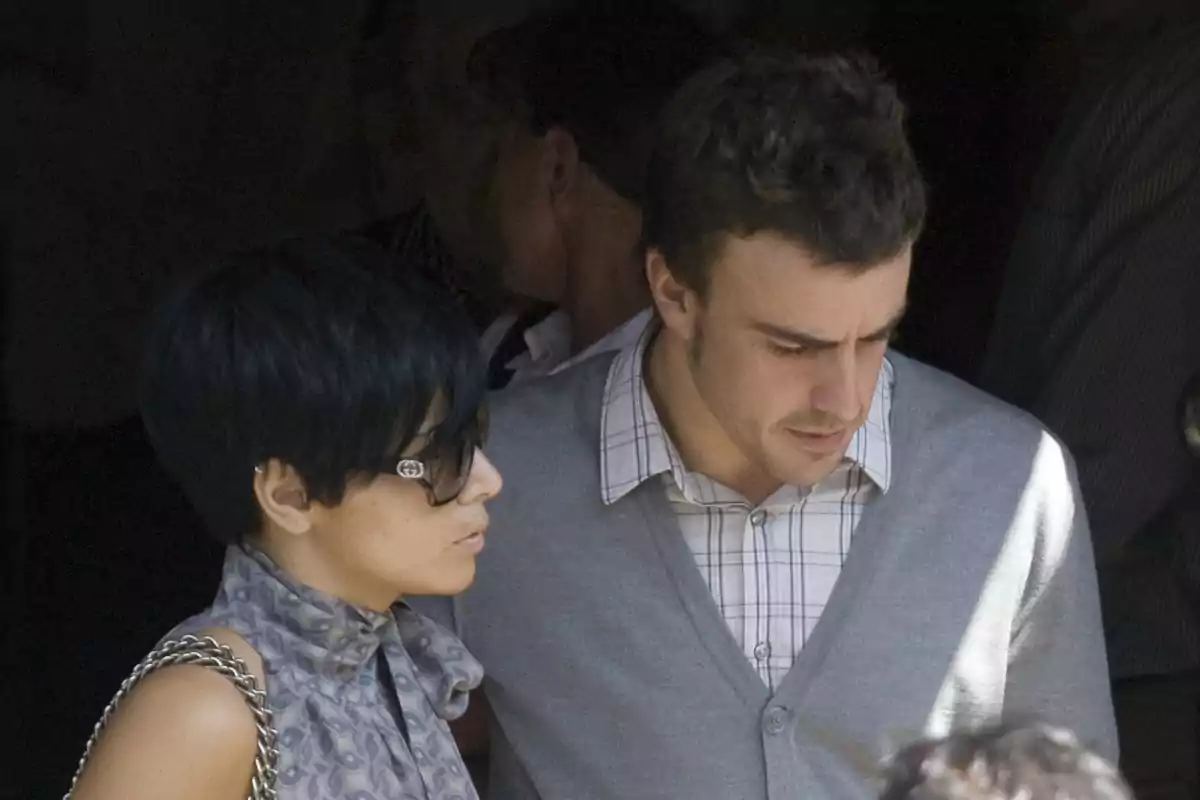 Raquel del Rosario and Fernando Alonso walking together, a woman with sunglasses and a man with a checkered jersey and gray sweater.