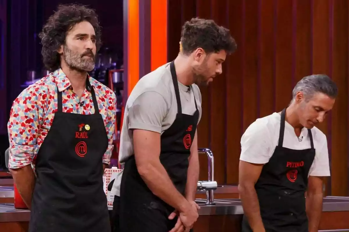 Raúl Gómez, José Lamuño i Pitingo amb davantals negres estan drets en una cuina de MasterChef Celebrity.