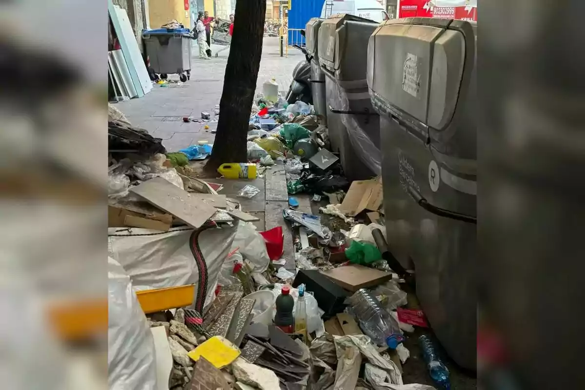 A sidewalk full of trash and debris next to recycling bins.