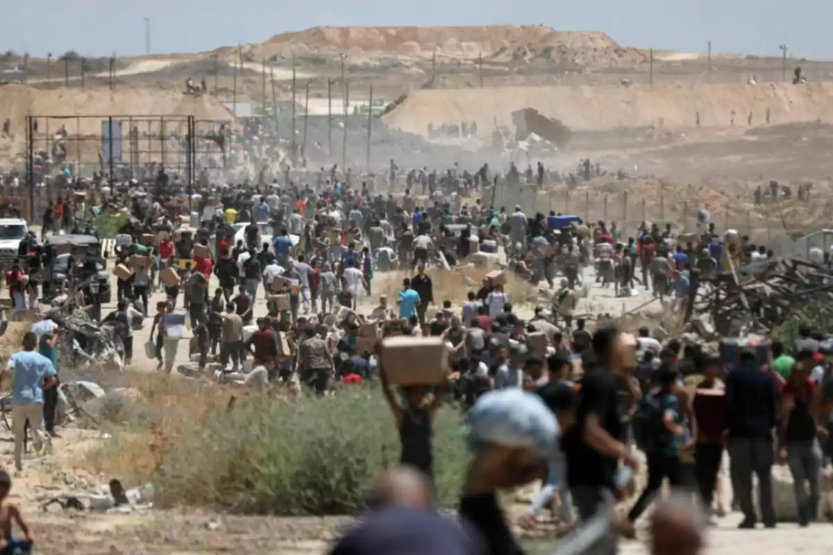 Multitud de persones caminant i carregant caixes en una zona desèrtica amb turons al fons i ambient polsós Multitud de persones caminant i carregant caixes en una zona desèrtica amb turons al fons i ambient polsós