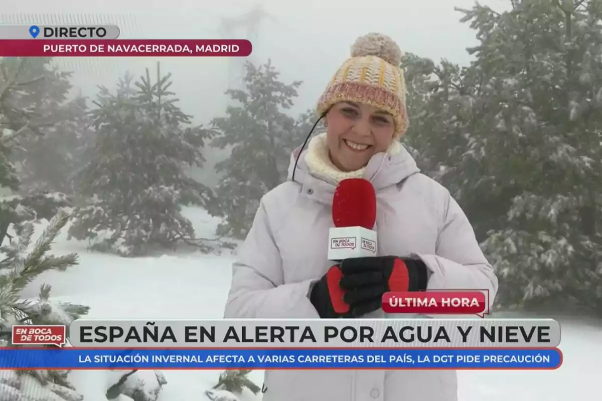 Reportera al Port de Navacerrada, Madrid, informant sobre l'alerta a Espanya per aigua i neu, amb un fons d'arbres nevats i un micròfon vermell d'En Boca de Todos a la mà. Reportera al Port de Navacerrada, Madrid, informant sobre l'alerta a Espanya per aigua i neu, amb un fons d'arbres nevats i un micròfon vermell d'En Boca de Todos a la mà.