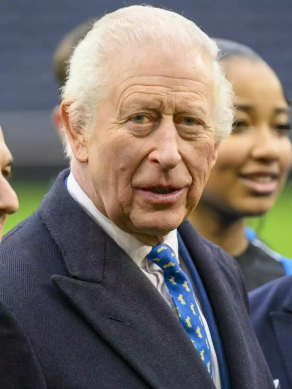 King Charles III with gray hair and a dark suit joined by other people.