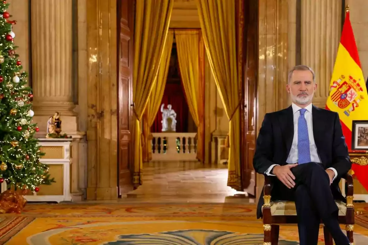 Felip VI assegut en una cadira en un saló elegant decorat amb un arbre de Nadal i una bandera d'Espanya.