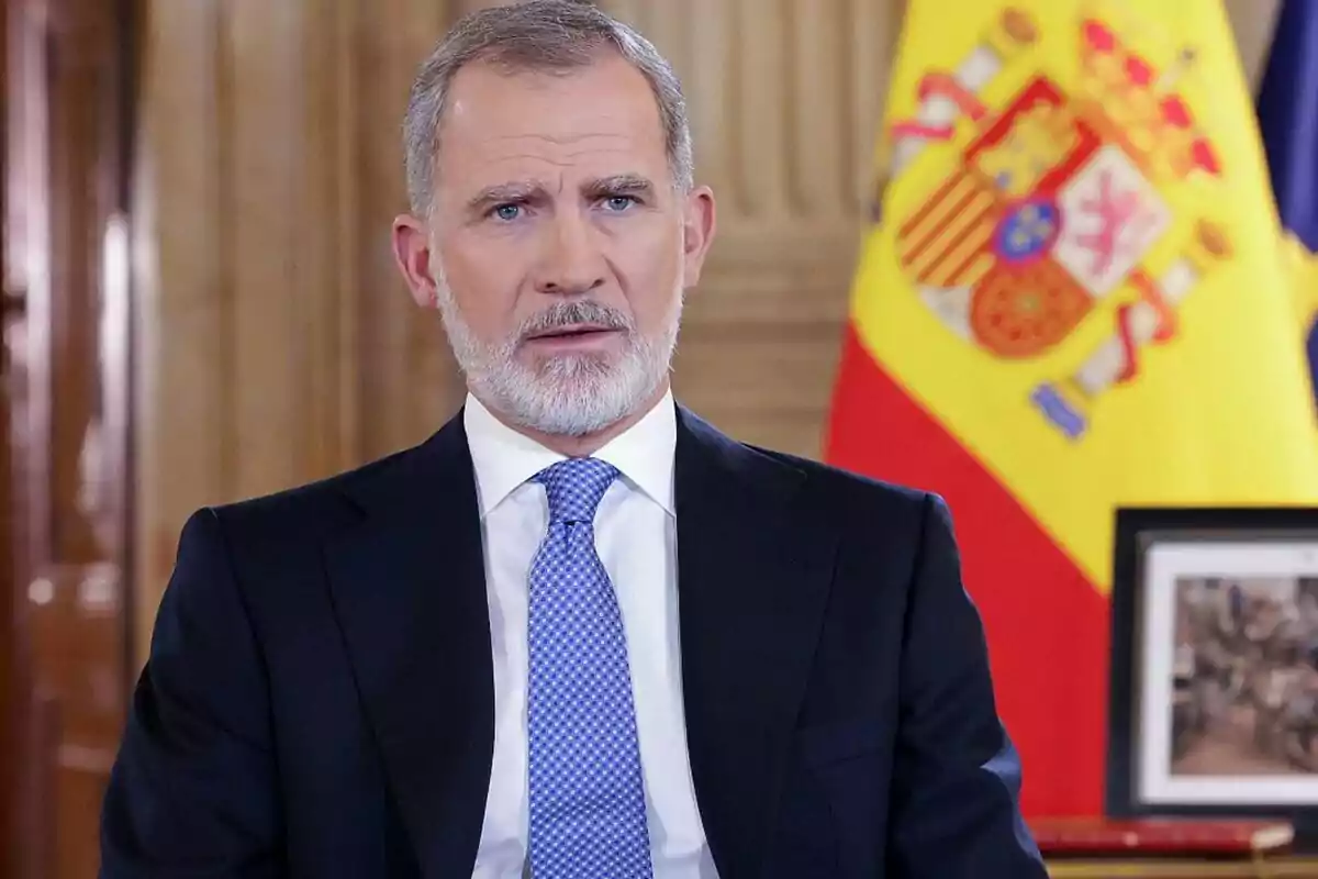 Felip VI amb barba i vestit fosc és davant d'una bandera d'Espanya.