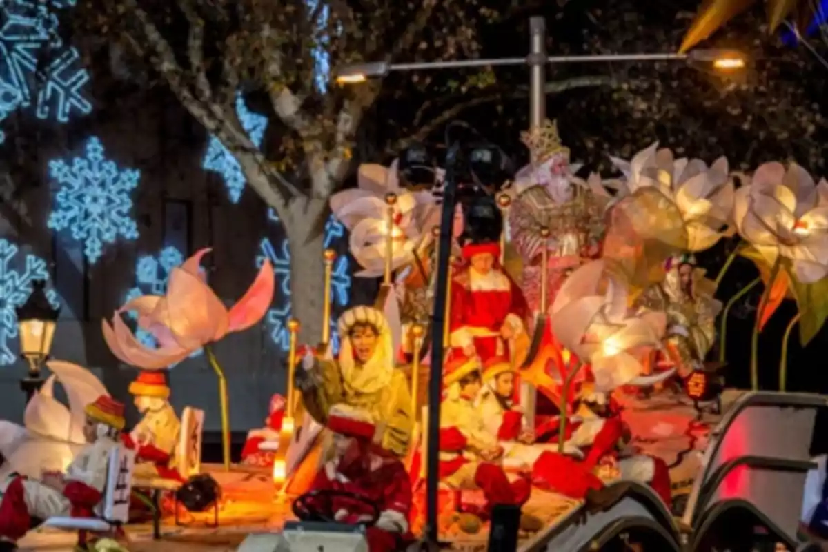 Desfile nocturno con carroza iluminada decorada con flores gigantes y figuras navideñas, rodeada de luces en forma de copos de nieve.