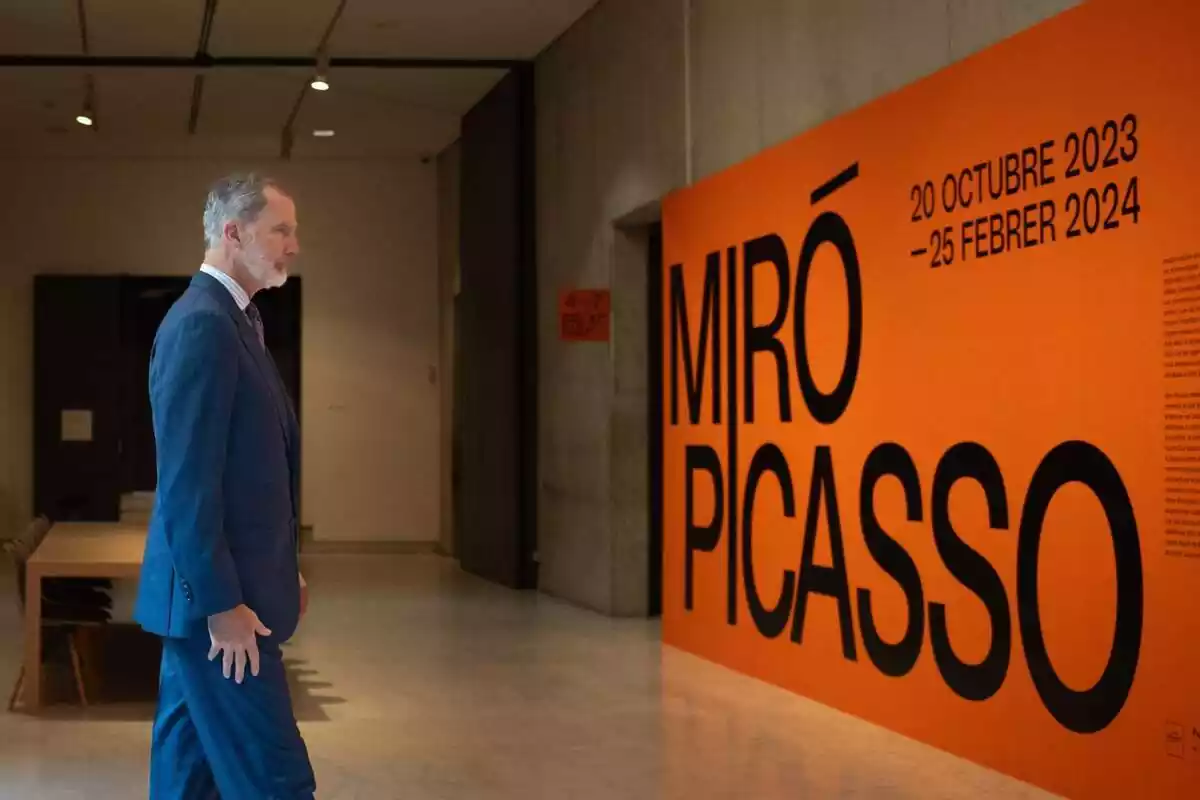 Pla americà del rei Felip de perfil mirant un cartell taronja amb els noms de Miró i Picasso