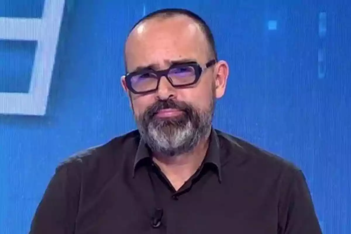 Risto Mejide amb barba i ulleres a Todo es Mentira amb fons blau.