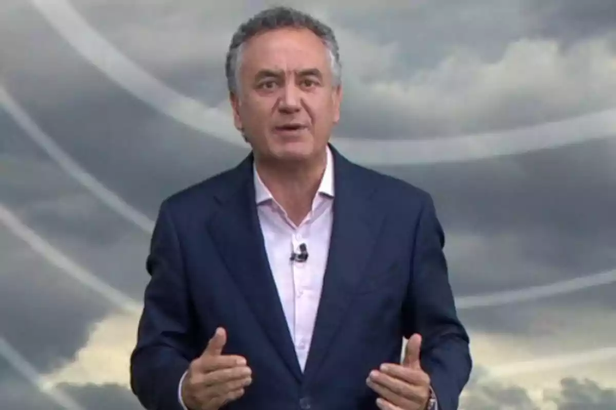 Pla mitjà de Roberto Brasero vestit amb un vestit blau i camisa clara parlant davant d’un fons de núvols grisos.