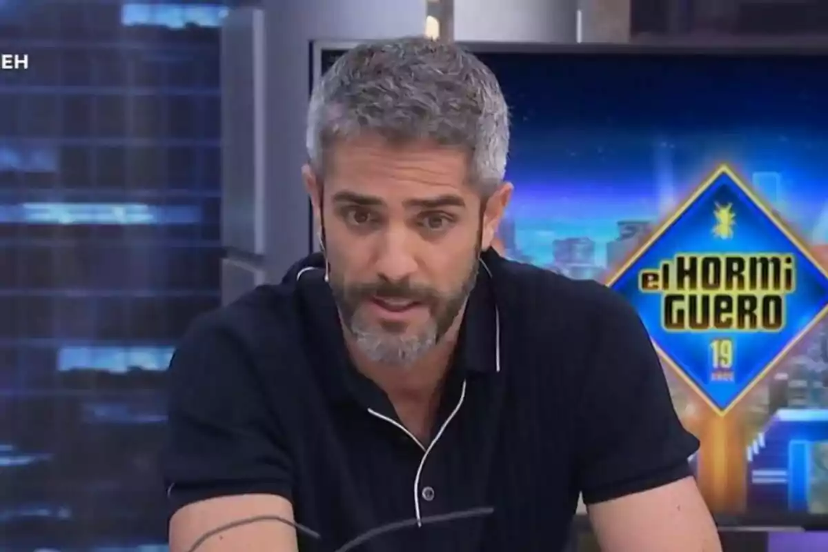 Roberto Leal de cabells canosos i barba parlant en un programa de televisió amb el logotip d’El Hormiguero al fons