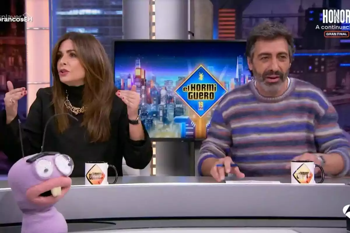 Nuria Roca i Juan del Val asseguts en un plató de televisió amb una titella i tasses amb el logotip de "El Hormiguero" a la taula.