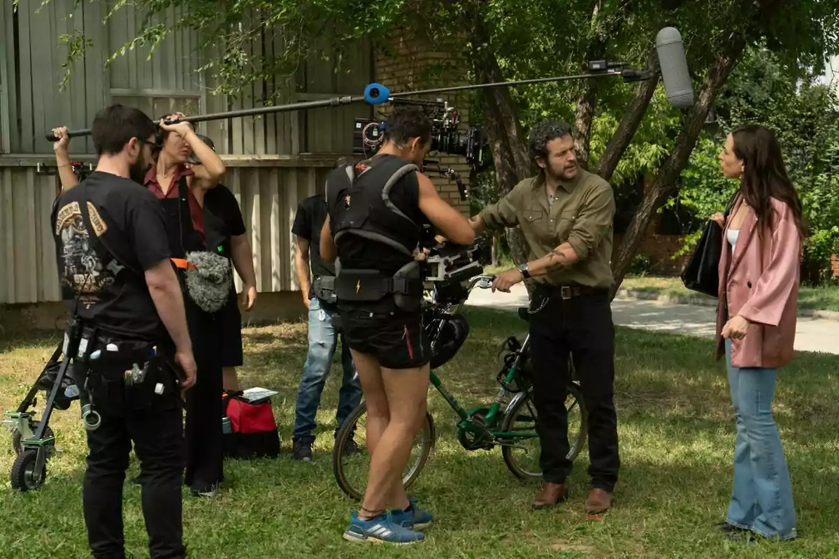 Equip de rodatge gravant una escena a l’aire lliure amb dos actors dialogant mentre l’equip tècnic sosté una càmera i un micròfon boom a la nova sèrie de comèdia ‘Sense Gluten’ de RTVE. Equip de rodatge gravant una escena a l’aire lliure amb dos actors dialogant mentre l’equip tècnic sosté una càmera i un micròfon boom a la nova sèrie de comèdia ‘Sense Gluten’ de RTVE.