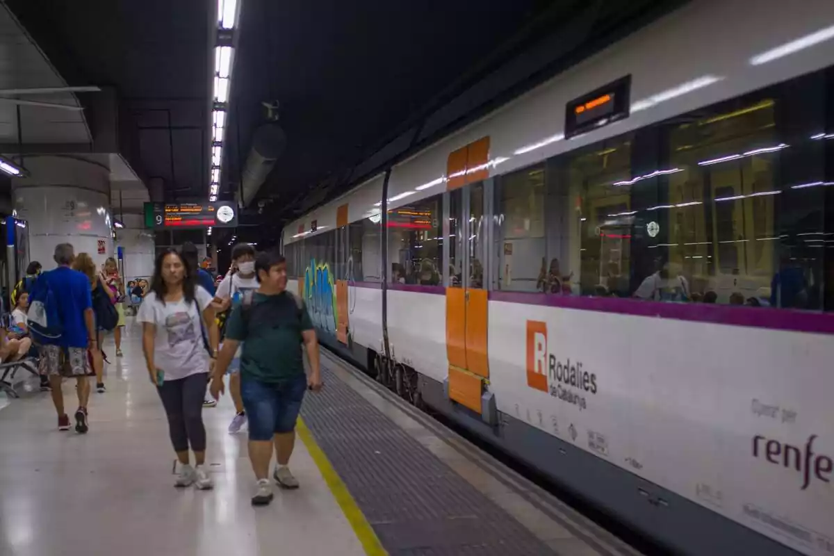 Imatge d'un tren de Rodalies aturat i diversos usuaris caminant i esperant a l'andana