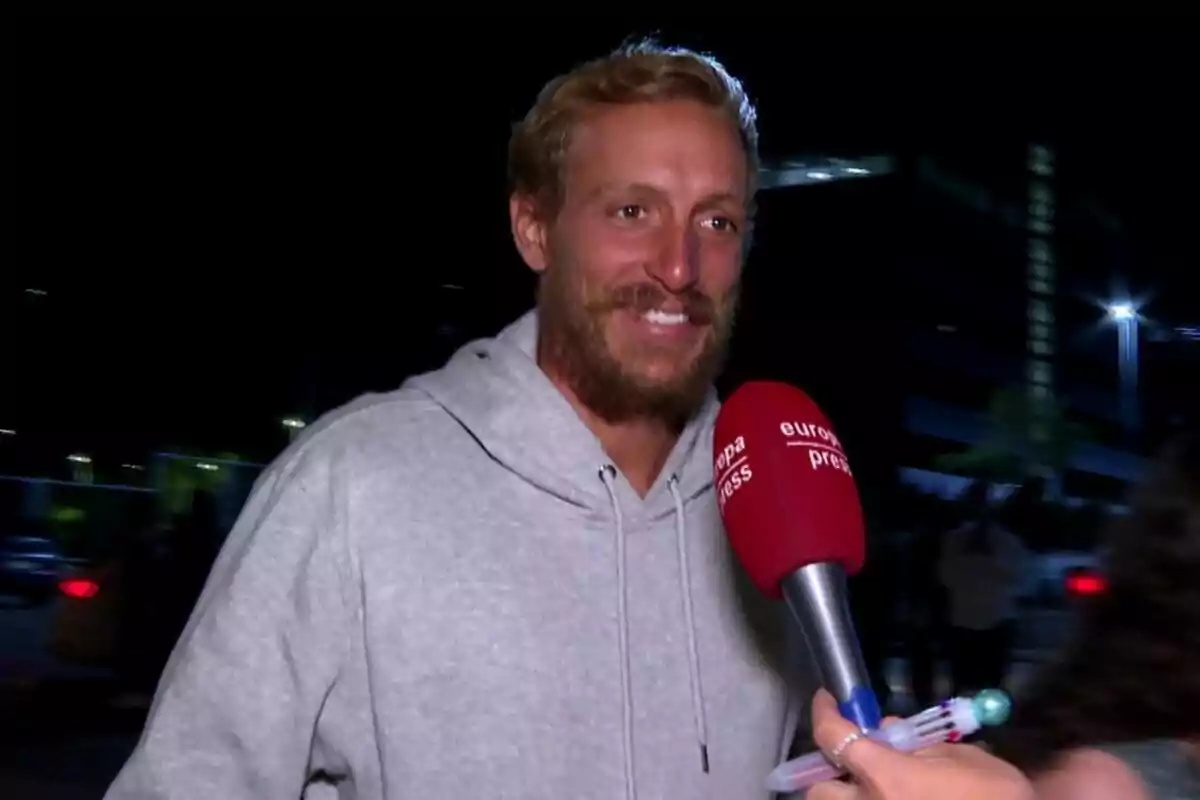 Rubén Torres sonriendo en sudadera gris con un micrófono rojo delante