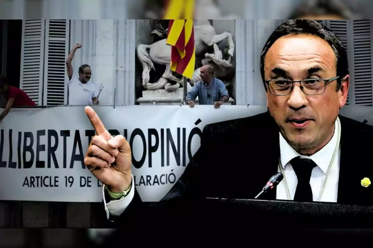 A man with glasses and a suit speaks into a microphone while pointing his finger, in the background there is a banner that says "Freedom of opinion" and people holding it.