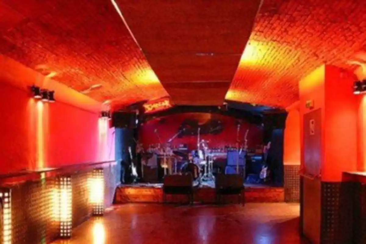 Sala de concerts amb una il·luminació vermella i al final un escenari amb micròfons, una bateria i guitarres