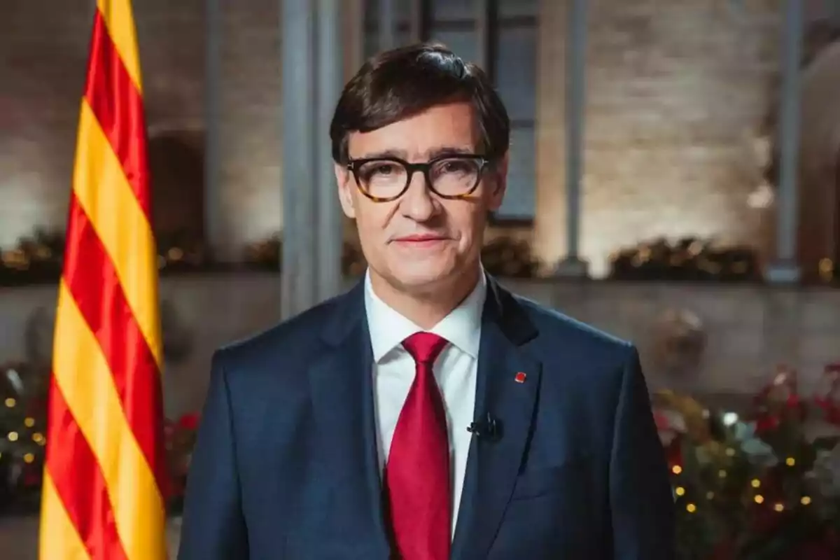 Home amb vestit i corbata vermella davant d'una bandera catalana en un entorn formal.