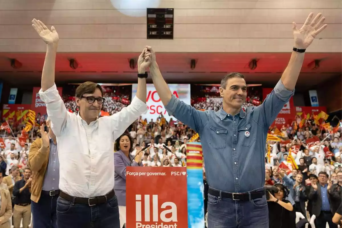 Salvador Illa i Pedro Sánchez agafats de la mà amb rostre somrient en un acte del PSC