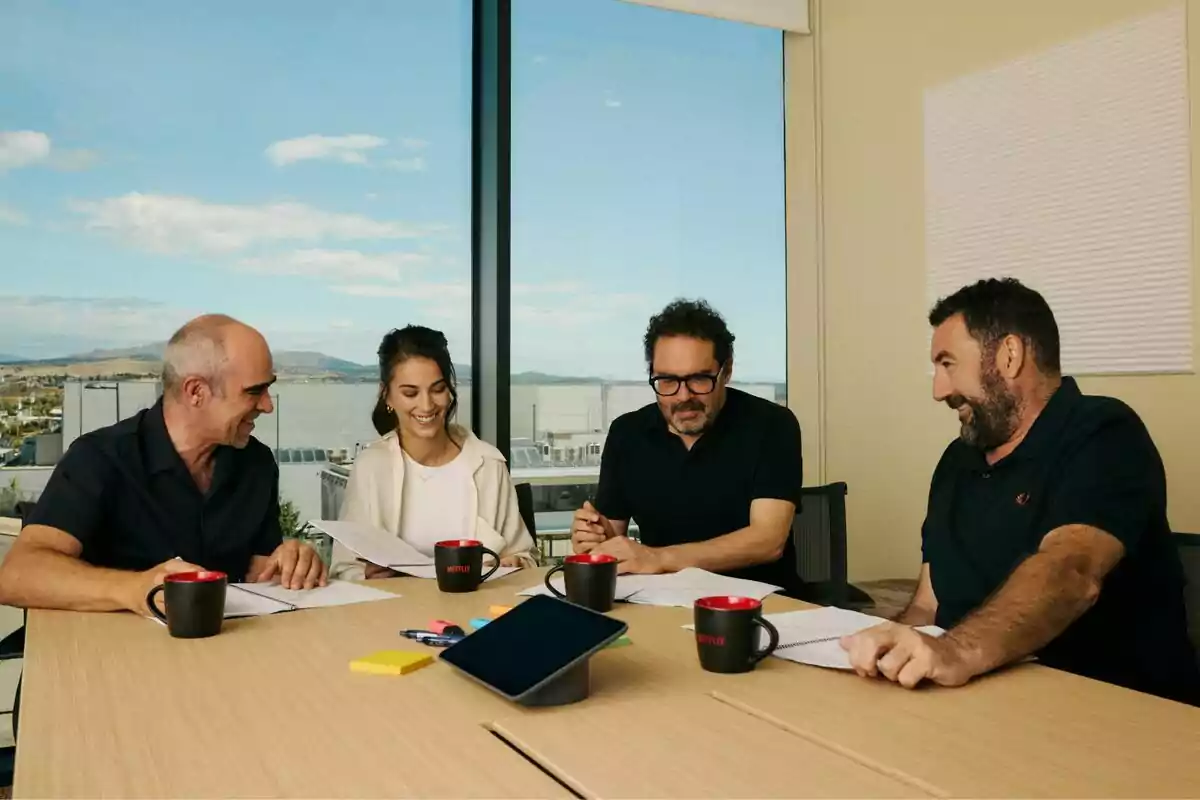 Fotografía de Fotografía de Aitor Gabilondo, Luis Tosar, Claudia Salas y Daniel Calparsoro sentadas alrededor de una mesa en una sala de reuniones con ventanas grandes y una vista panorámica, revisando documentos y sonriendo en el rodaje de Salvaje