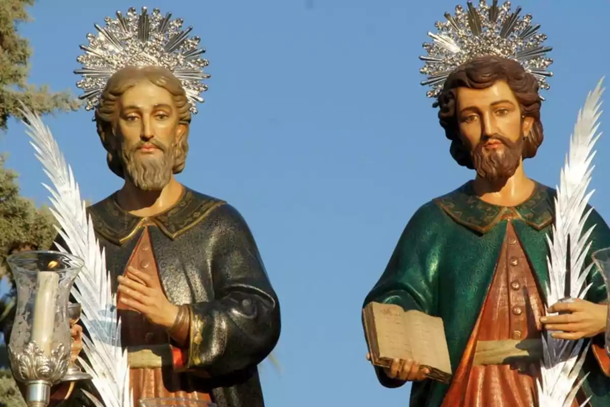 Dues estàtues religioses amb aurèoles i palmells, una sostenint una espelma i l'altra un llibre, amb un fons de cel blau.