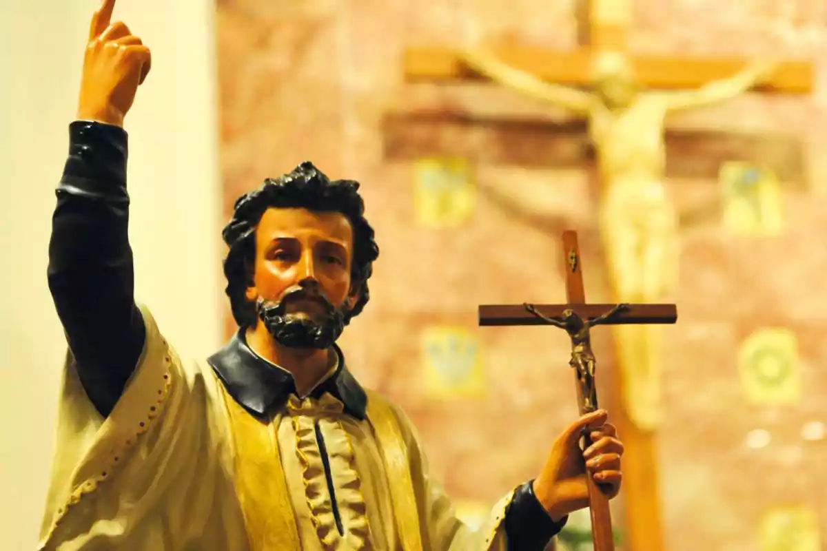 Estàtua d´un sant sostenint un crucifix amb un fons d´una creu gran.