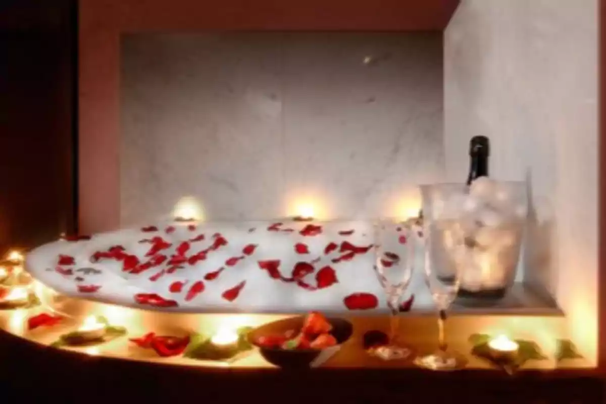 Bathtub with rose petals, lit candles, champagne glasses, and strawberries in a romantic setting.