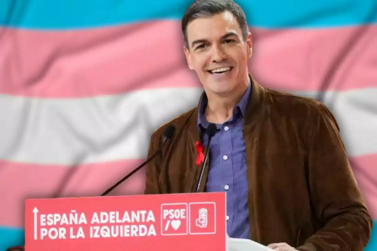 Un home somrient en un podi amb un cartell que diu "Espanya avança per l'esquerra" i el logotip del PSOE, amb una bandera de colors al fons.