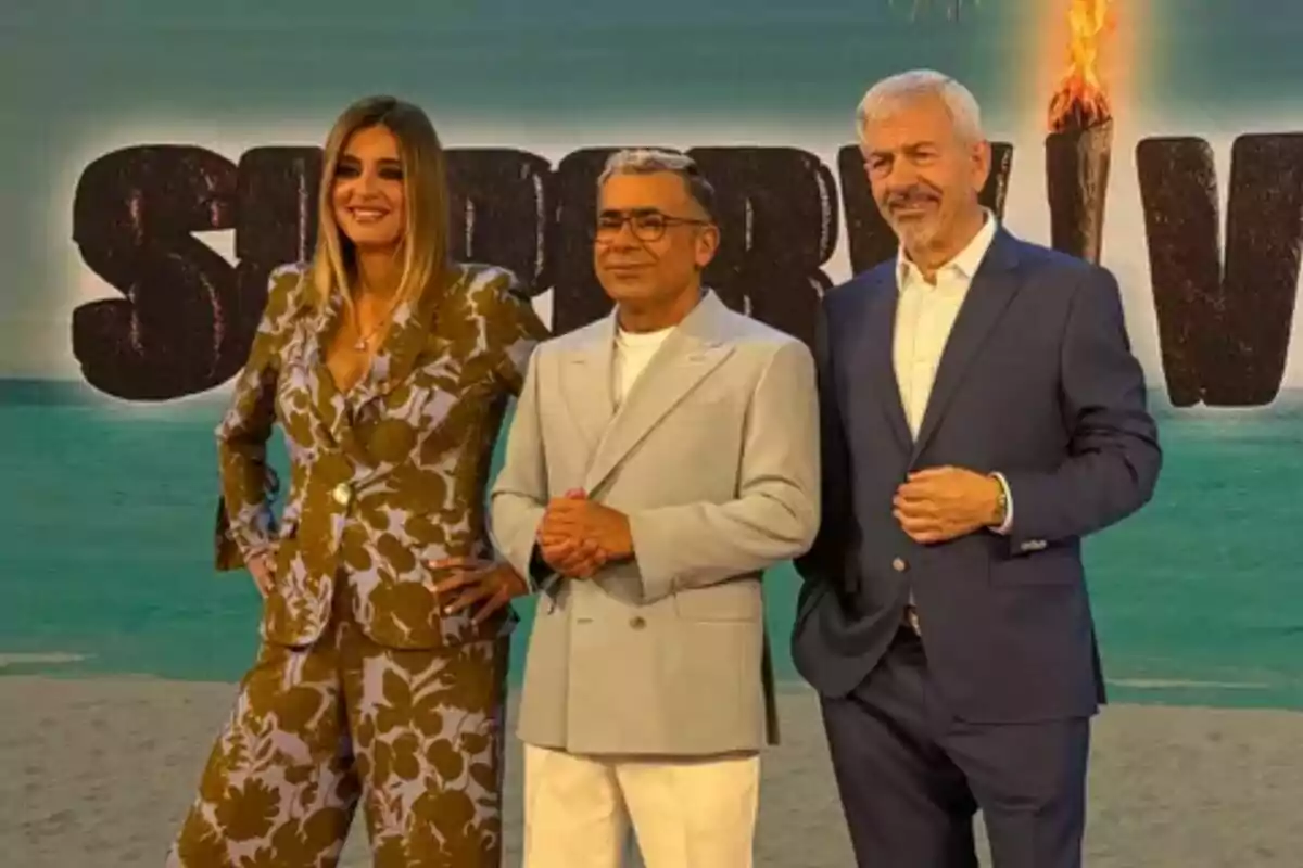 Sandra Barneda, Jorge Javier Vázquez y Carlos Sobera posan frente a un cartel con letras grandes de Supervivientes con una antorcha encendida.