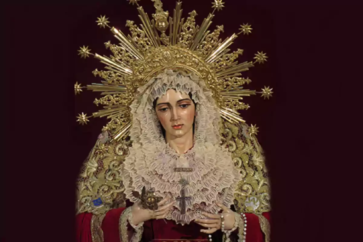 Imatge d’una figura religiosa de la Mare de Déu vestida amb un mantell brodat en daurat i un tocador de puntes, amb una corona daurada decorada amb raigs i estrelles sobre un fons fosc. Imatge d’una figura religiosa de la Mare de Déu vestida amb un mantell brodat en daurat i un tocador de puntes, amb una corona daurada decorada amb raigs i estrelles sobre un fons fosc.