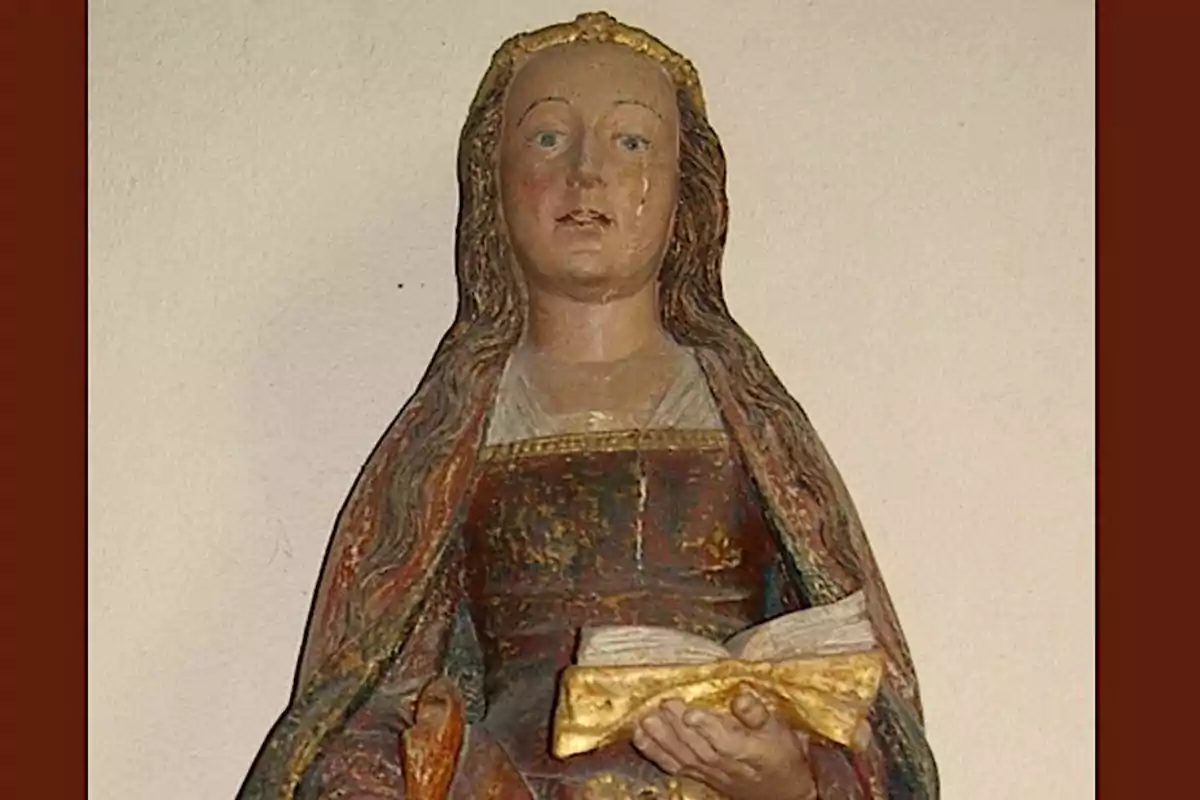 Escultura d'una figura femenina amb cabell llarg i solt sostenint un llibre obert a les seves mans.