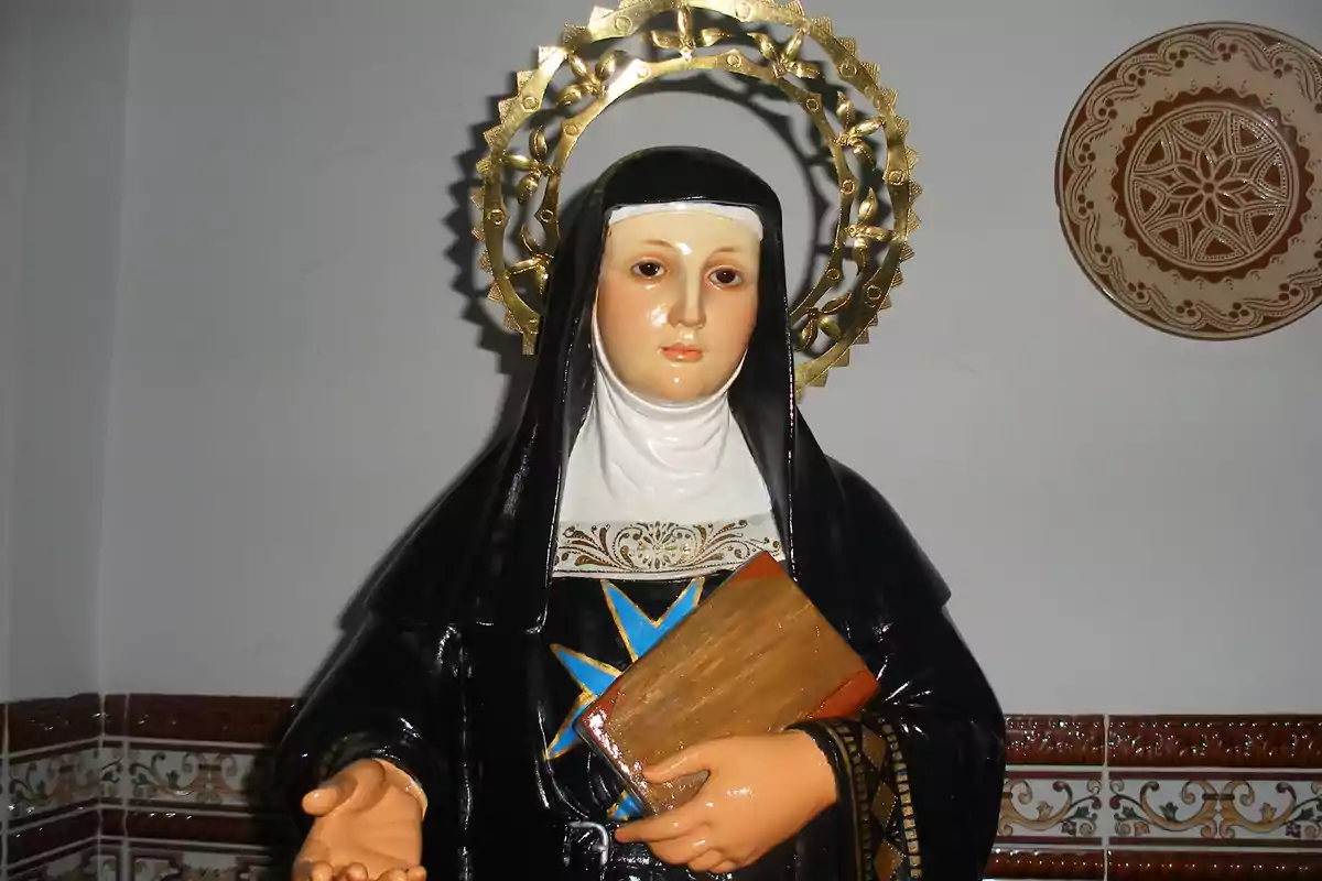 Una estàtua religiosa d'una figura femenina amb hàbit negre i un halo daurat sostenint un llibre en una mà. Una estàtua religiosa d'una figura femenina amb hàbit negre i un halo daurat sostenint un llibre en una mà.