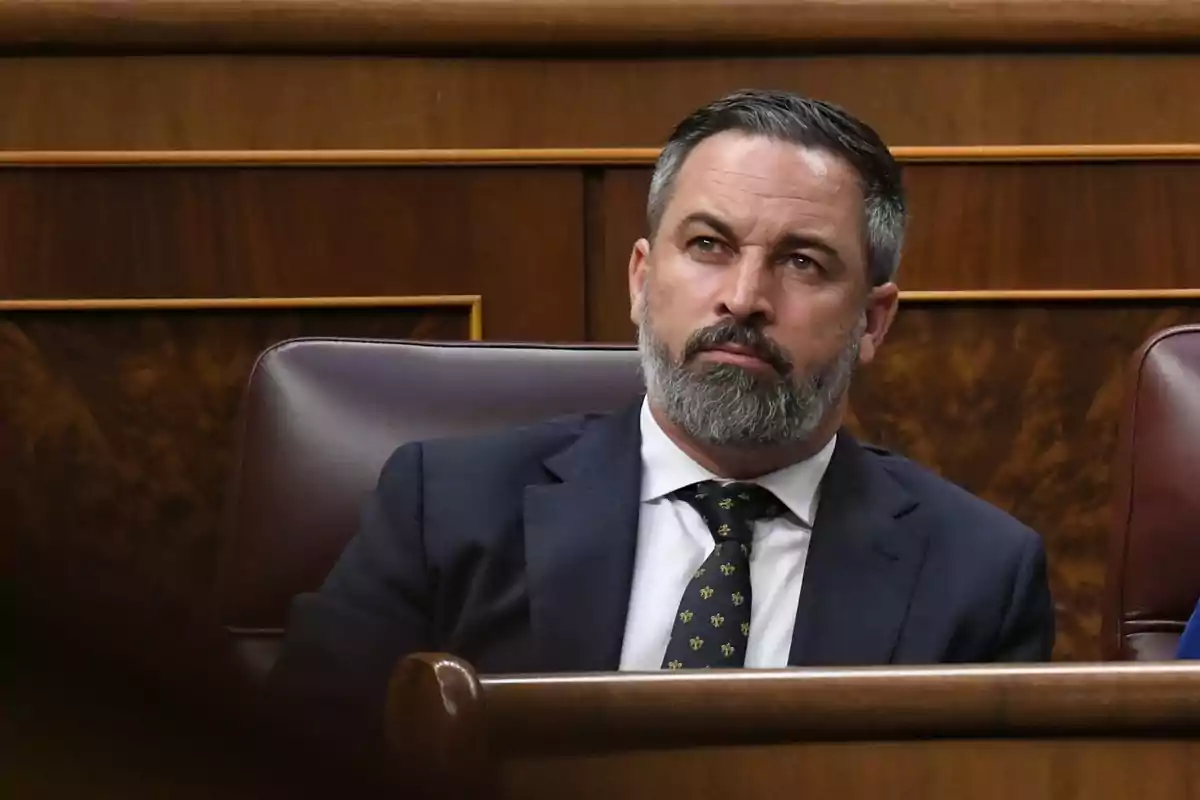 Bearded man in a suit sitting on a leather seat in a wooden setting.