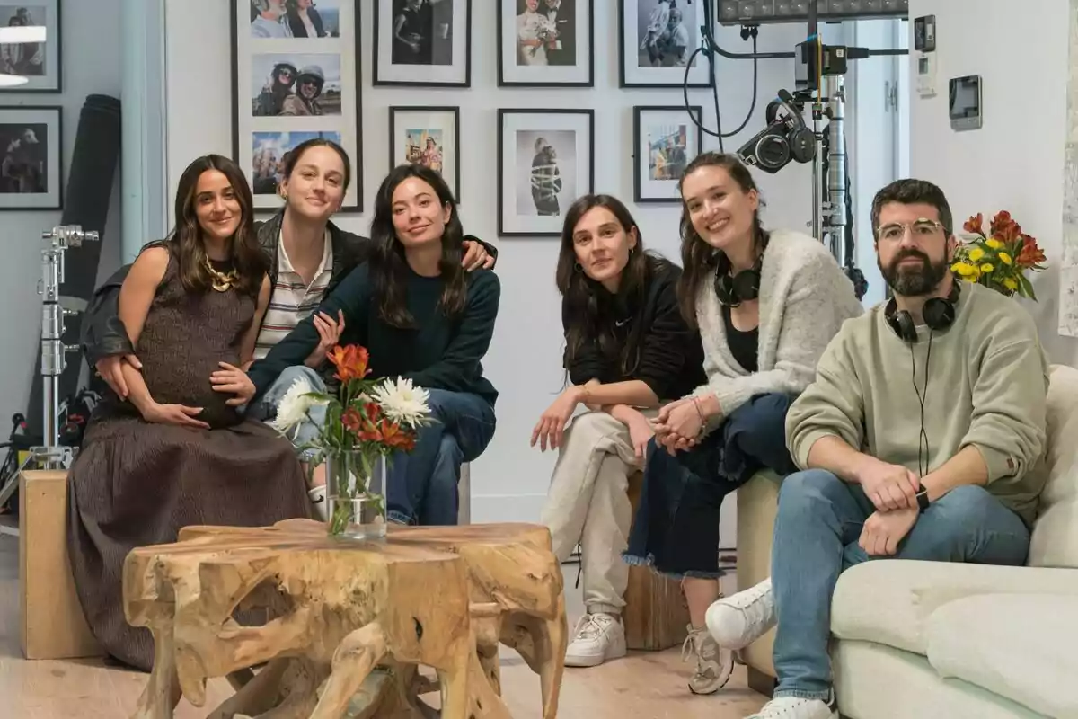 Anna Castillo, Macarena García, Laura Weissmahr, Victoria Martín, Sandra Romero i Nacho Pardo assegudes en una sala moderna amb parets decorades amb fotografies i equip de gravació al fons, totes somriuen i semblen relaxades, al centre hi ha una taula de fusta amb un gerro durant el rodatge de S’ha de morir molta gent.