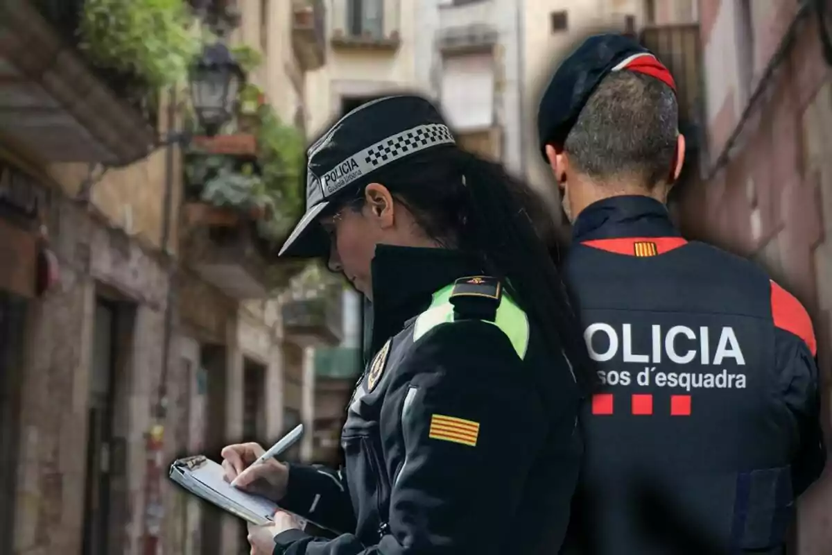 Two uniformed police officers, one writing in a notepad and the other with their back turned, on an urban street.