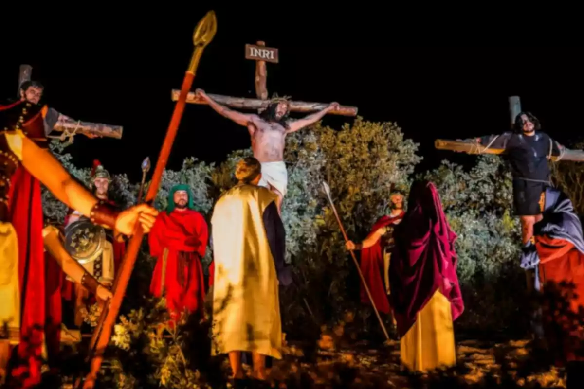 Una representación teatral de la crucifixión con actores vestidos con trajes históricos y cruces iluminadas en un entorno nocturno.