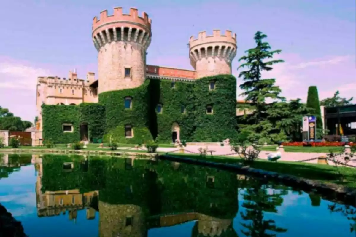 Un castell amb torres cobertes d’heura reflectit en un estany.