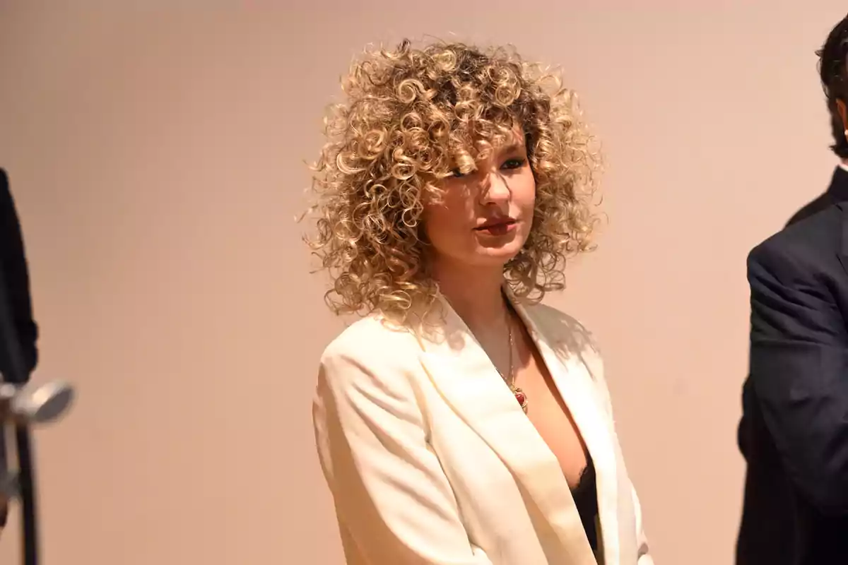 Sheila Casas with curly blonde hair wears a white suit at a formal event. Sheila Casas with curly blonde hair wears a white suit at a formal event.