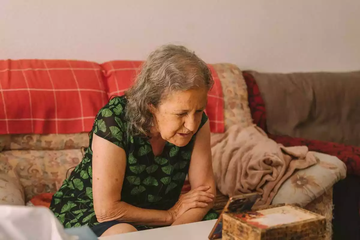 Imatge d'una dona gran, asseguda en un sofà, parlant amb algú a través d'un mòbil per trucada de vídeo