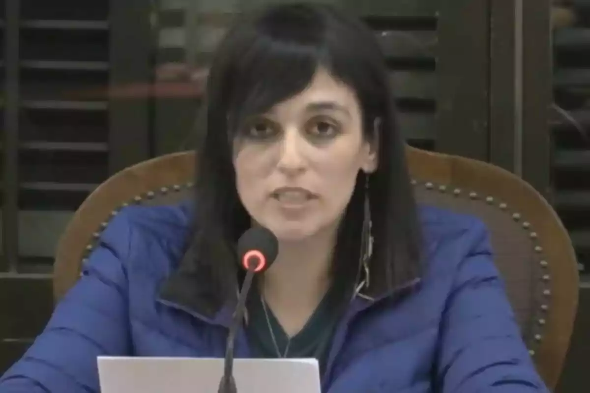 A person in a blue jacket speaks in front of a microphone in a conference room.