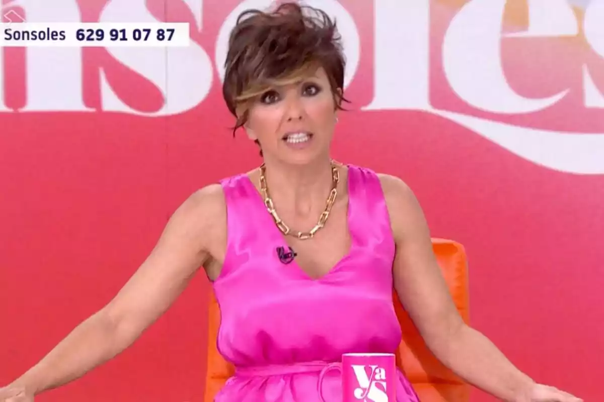 Sonsoles Ónega amb vestit rosa i collaret daurat asseguda a 'Y ahora Sonsoles' amb fons vermell i una tassa rosa sobre la taula