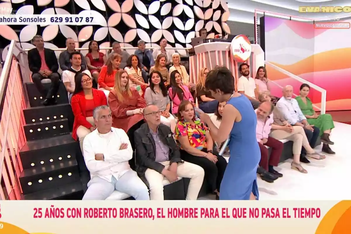 El públic està assegut a 'Y ahora Sonsoles', mentre Sonsoles Ónega interactua amb el públic; el fons té un disseny geomètric i hi ha un missatge a la part inferior que esmenta Roberto Brasero. El públic està assegut a 'Y ahora Sonsoles', mentre Sonsoles Ónega interactua amb el públic; el fons té un disseny geomètric i hi ha un missatge a la part inferior que esmenta Roberto Brasero.