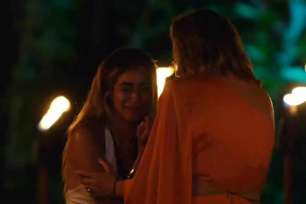 Sthefany y Sandra Barneda interactuando en un ambiente iluminado por antorchas, una de ellas parece estar consolando a la otra en La Isla de las Tentaciones.