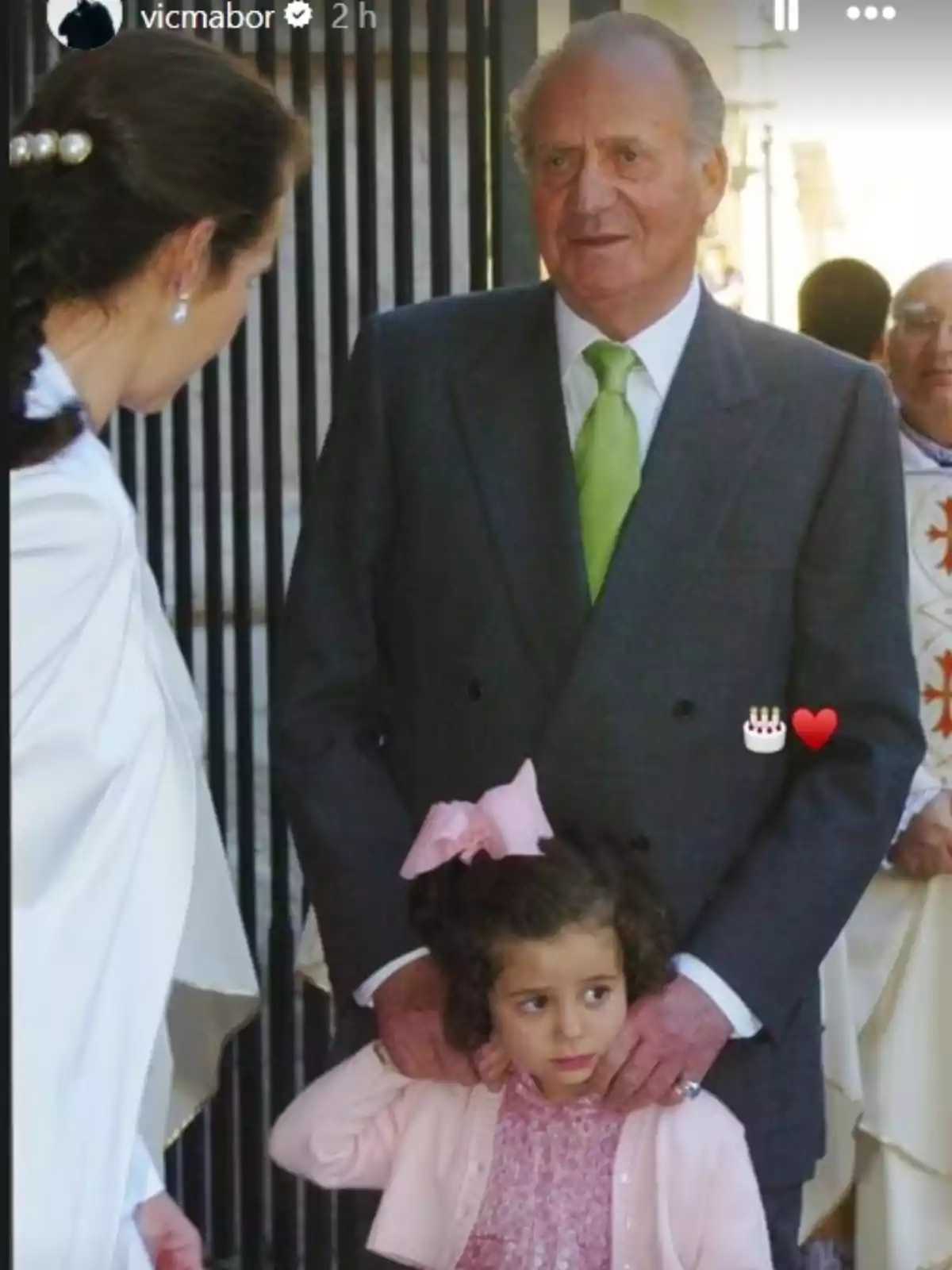 Story de Victoria Federica donde ella aparece de niña y con un lazo rosa en el pelo mientras la acaricia Juan Carlos I, con traje gris y corbata verde, siendo observados por la infanta Elena que aparece de espaldas con traje blanco