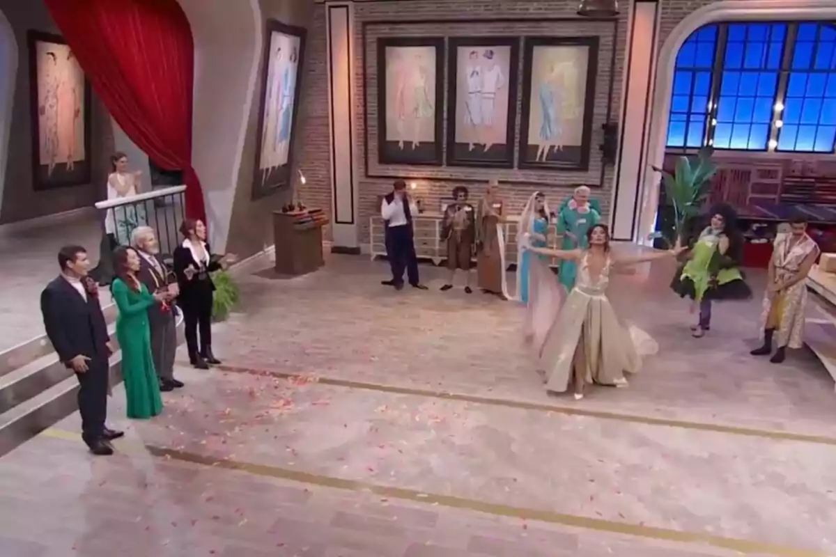 Els concursants de 'Maestros de la Costura Celebrity' elegantament vestits es troben en un saló ampli amb decoracions artístiques a les parets, mentre una dona al centre sembla estar realitzant una presentació o ball, envoltada de pètals a terra. Els concursants de 'Maestros de la Costura Celebrity' elegantament vestits es troben en un saló ampli amb decoracions artístiques a les parets, mentre una dona al centre sembla estar realitzant una presentació o ball, envoltada de pètals a terra.