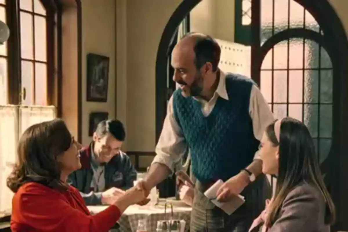 Gaspar sonriente saluda a Manuela en un restaurante acogedor mientras Claudia observa la escena. Captura de 'sueños de libertad'