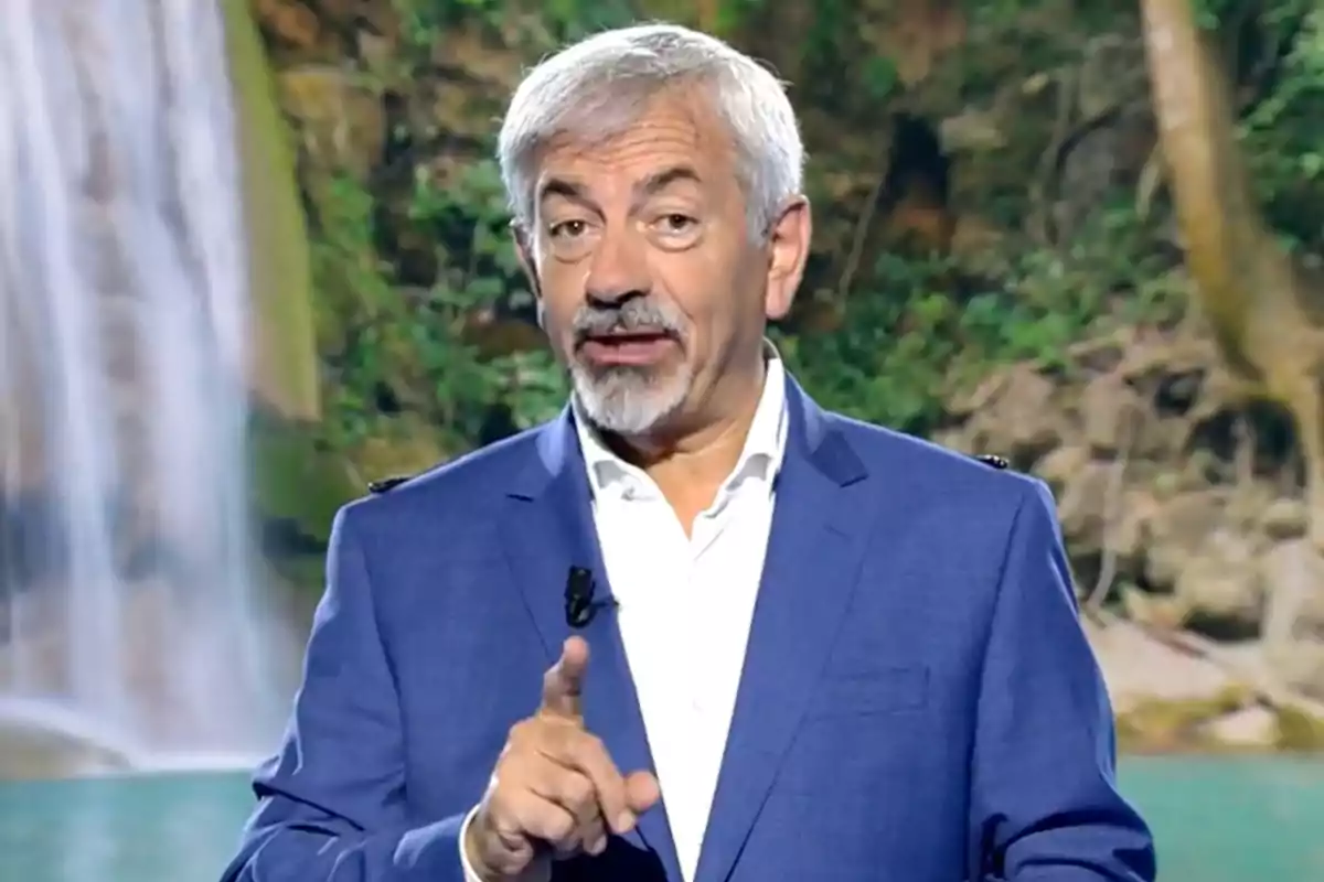 Carlos Sobera dressed in a blue blazer and white jersey speaking in front of a backdrop of a waterfall and vegetation. Screenshot from 'Supervivientes' Carlos Sobera dressed in a blue blazer and white jersey speaking in front of a backdrop of a waterfall and vegetation. Screenshot from 'Supervivientes'